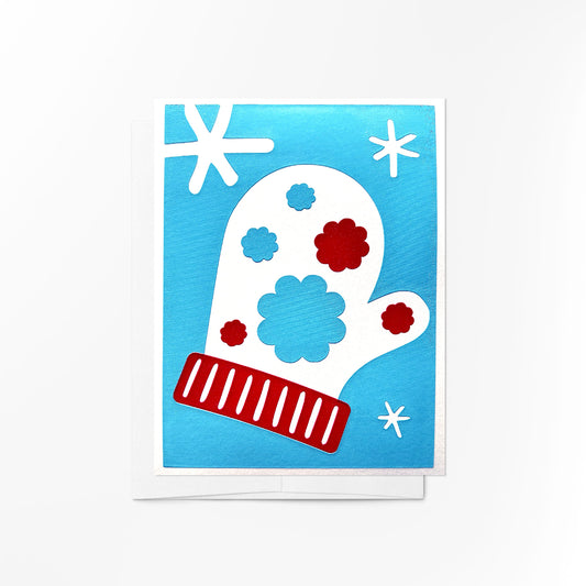 A handcrafted greeting card featuring a red-and-white mitten adorned with delicate snowflakes and floral accents, capturing the cozy essence of winter.