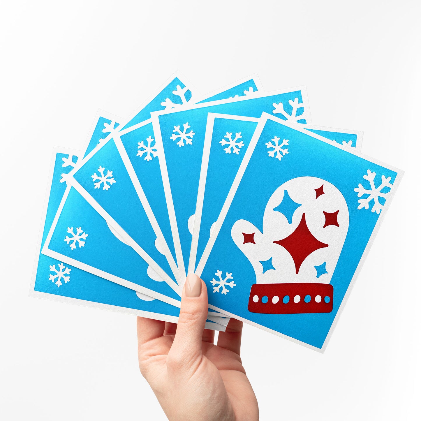 A hand holding a fan of Starry Mitten Cards, showcasing the vibrant blue background , cozy mitten, and white snowflakes. Perfect for sharing festive holiday greetings.