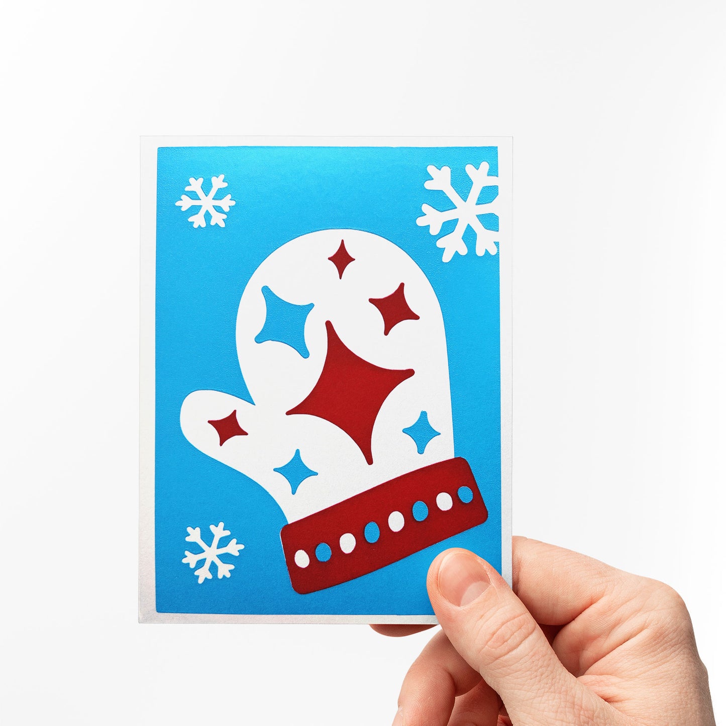 A hand holding the Starry Mitten Card, featuring a vibrant blue background with a festive red and white mitten design, accented by twinkling stars and snowflakes. Perfect for celebrating the cozy magic of winter holidays.