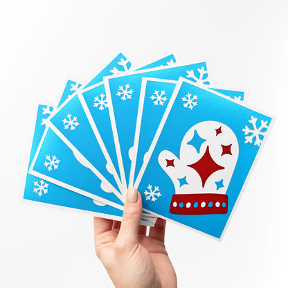  A hand holding a fan of Starry Mitten Cards, showcasing the vibrant blue  background , cozy mitten, and white snowflakes. Perfect for sharing festive holiday greetings.