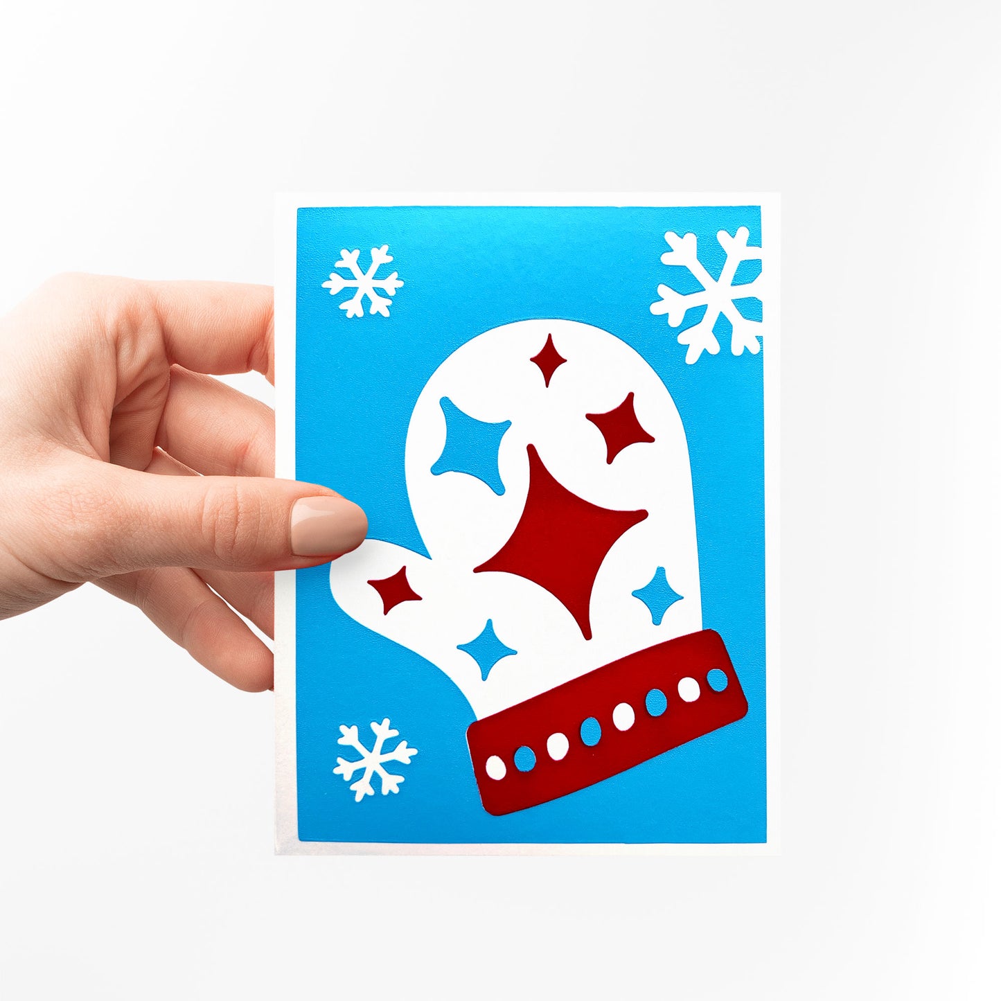 A hand holding the Starry Mitten Card, highlighting its festive blue background with a red and white mitten design adorned with twinkling stars and snowflakes. Perfect for spreading holiday warmth.