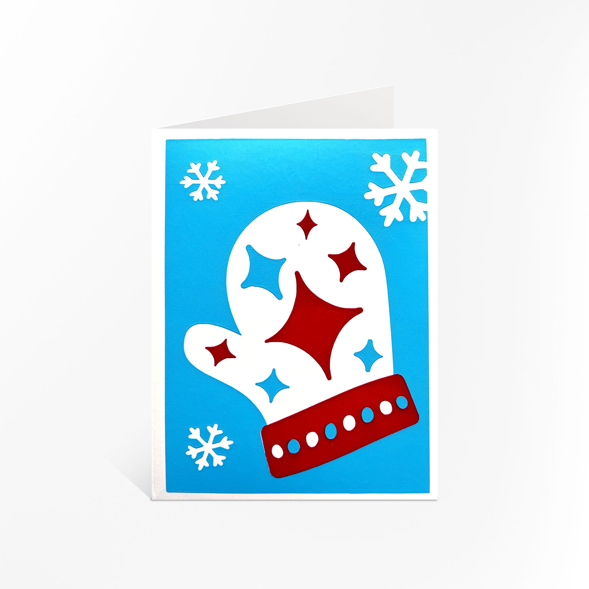 The Starry Mitten Card displayed upright, featuring a festive blue background with a red and white mitten adorned with stars and surrounded by snowflakes. A cheerful and cozy holiday card from McWu’s collection.