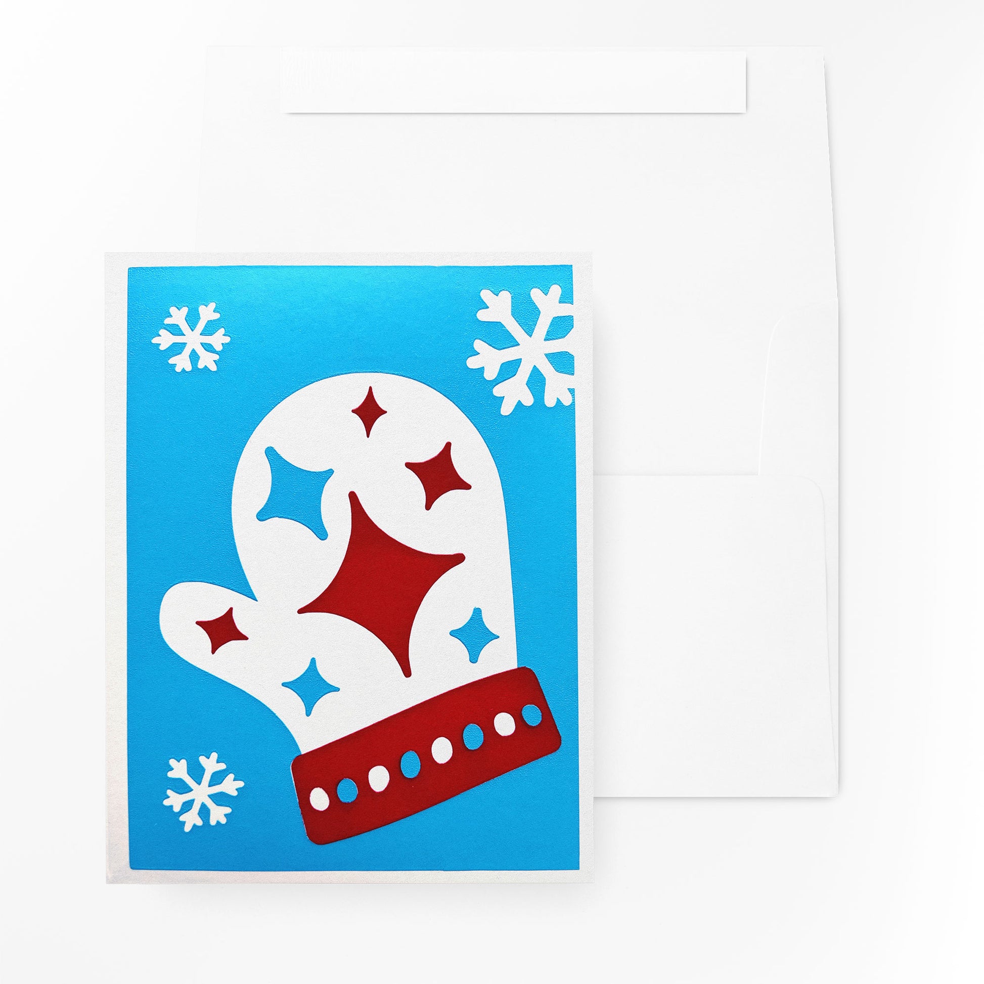 The Starry Mitten Card displayed alongside its matching white envelope, showcasing its vibrant blue background with a red and white mitten design accented by twinkling stars and snowflakes. A festive holiday card ready for gifting.